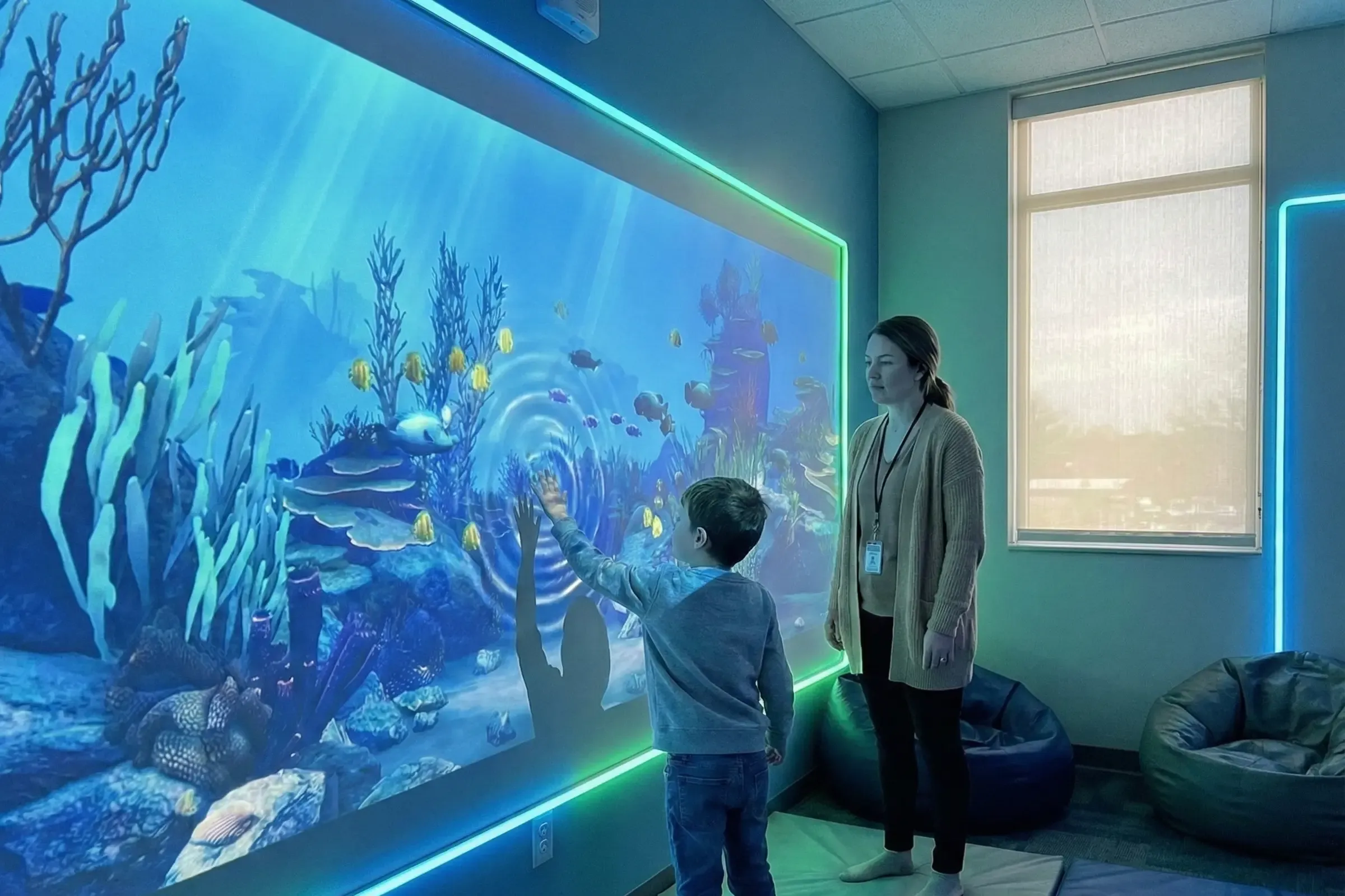 Child in sensory room touching underwater projection wall with therapist