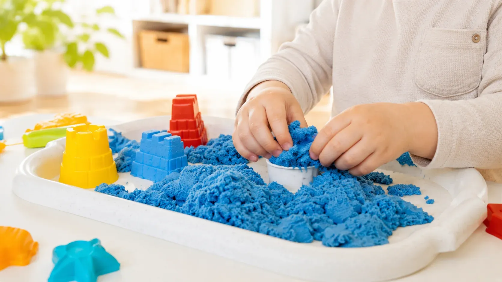 A child plays with kinetic sand at a tactile sensory table, scooping and shaping the material for hands-on textural input