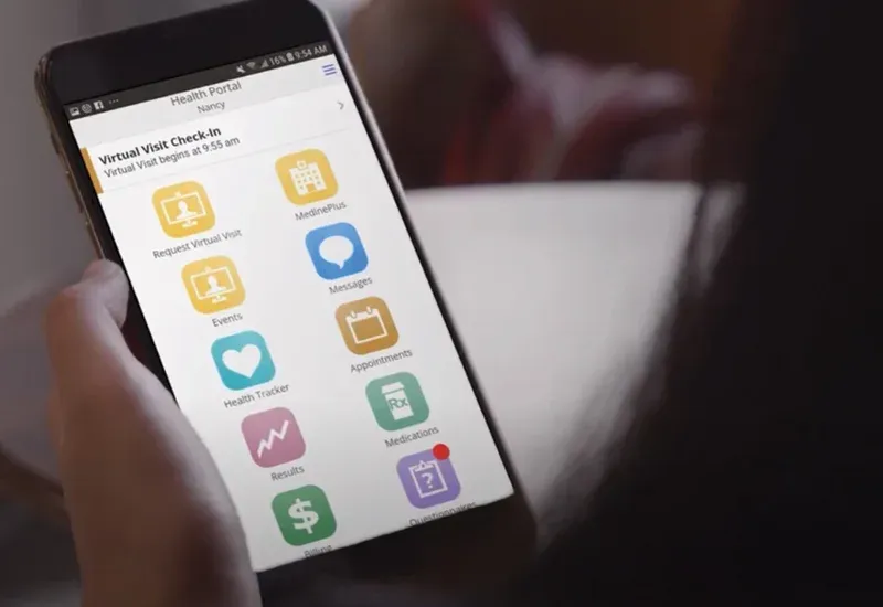 A patient using the MEDITECH MHealth app on a smartphone to check in for a virtual visit and access health portal features