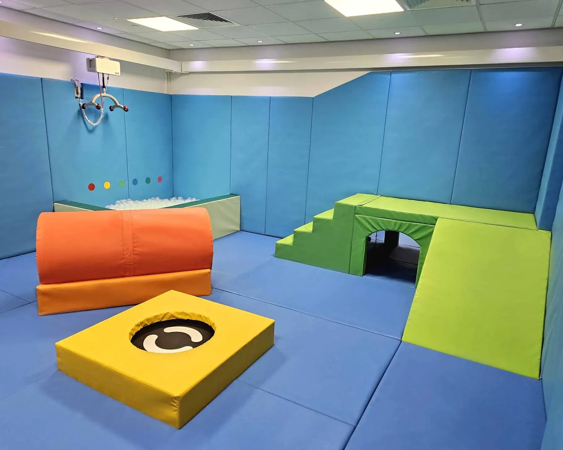 A padded school sensory circuit room with foam crash pads, soft play obstacles, and pastel-blue walls