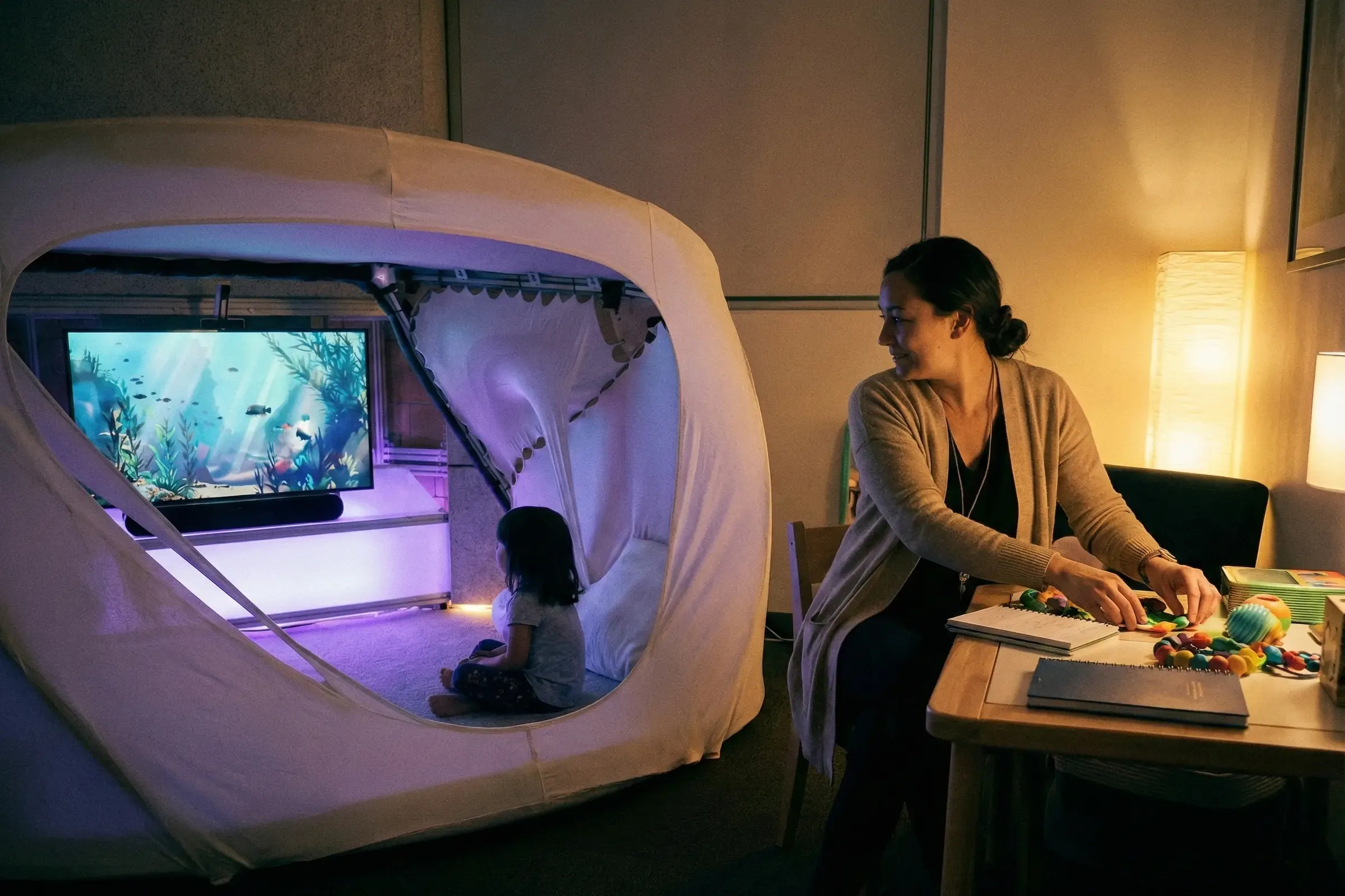 A child resting in a sensory cocoon at home while a parent observes nearby, an example of a calm, choice-based environment